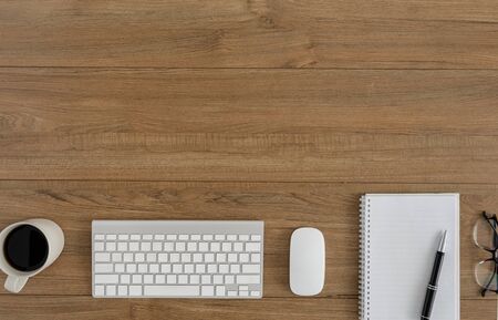 Flat lay, top view wooden office desk. Workspace with blank notebook, mouse computer, keyboard, pen, eye glasses, coffee cup office supplies with coppy space on wood table backgroundの写真素材