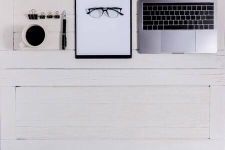 Flat lay, top view wooden office desk. Workspace with notebook, laptop, clipboard, pen, paper clip, eye glasses, coffee cup office supplies with coppy space on white wood table backgroundの写真素材