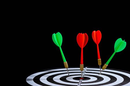 Red and green dart arrow hitting target center Dart board Isolated on blackの写真素材