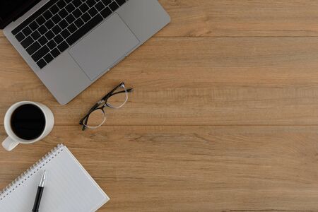 Flat lay, top view wooden office desk. Workspace with blank notebook, coffee cup, laptop, pen, eye glasses office supplies with coppy space on wood table backgroundの写真素材