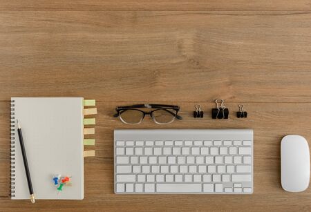 Flat lay, top view wooden office desk. Workspace with blank notebook, keyboard, mouse computer, pencil, metal clip, eye glasses office supplies with coppy space on wood table backgroundの写真素材
