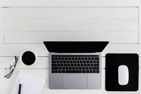 Flat lay, top view wooden office desk. Workspace with blank notebook, laptop, mouse computer, eye glasses, pen, coffee cup office supplies with coppy space on white wood table backgroundの写真素材