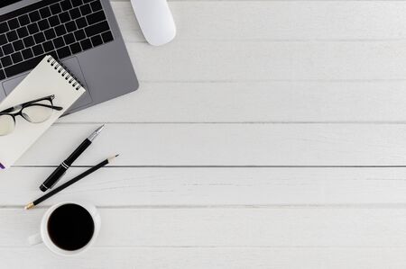 Flat lay, top view wooden office desk. Workspace with blank notebook, laptop, mouse computer, eye glasses, pen, coffee cup office supplies with coppy space on white wood table backgroundの写真素材
