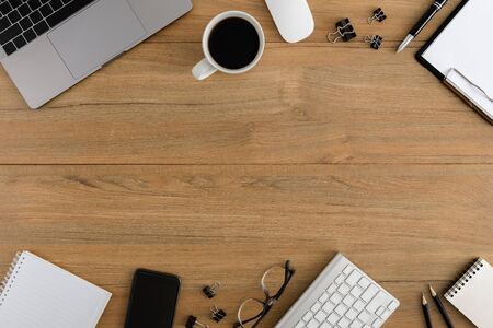 Flat lay, top view wooden office desk. Workspace with blank clipboard, laptop, smartphone, pen, eye glasses, metal clip, coffee cup office supplies with coppy space on wood table backgroundの写真素材