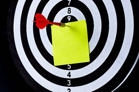 Red dart arrow hitting target center with blank sticky notes on Dart board on black background, Setting aim goal achievement concept challenging business goals, ready to achieve and Marketing conceptの写真素材