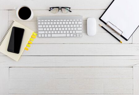 Flat lay, top view wooden office desk. Workspace with blank notebook, keyboard, mouse computer, smartphone, eye glasses, pencil, coffee cup office supplies with coppy space on white wood table backgroundの写真素材