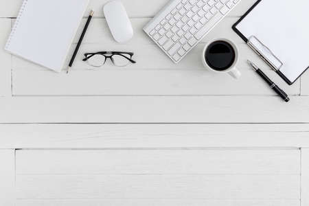 Flat lay, top view wooden office desk. Workspace with blank clipboard, keyboard, mouse computer, eye glasses, pen, coffee cup office supplies with coppy space on white wood table backgroundの写真素材