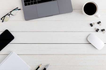 Flat lay, top view wooden office desk. Workspace with blank clipboard, laptop, mouse computer, smartphone, eye glasses, coffee cup office supplies with coppy space on white wood table backgroundの写真素材