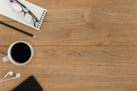 Flat lay, top view wooden office desk. Workspace with blank notebook, smartphone, earphones, pencil, eye glasses, coffee cup office supplies with coppy space on wood table backgroundの写真素材