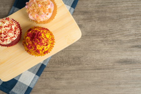 Top view of red velvet and strawberry cupcakes on wooden plate and napkin on wooden table top at top left corner of frameの写真素材