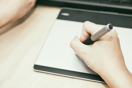 Retro image of female hand of a designer drawing with the stylus on a grey graphics tablet