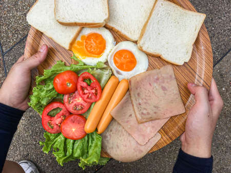 Fried eggs with bacon and grain bread on Wooden plate A man is having Breakfast. Bright yellow background. Eggs for Breakfast, proper nutrition. The view from the top. Hands close upの写真素材