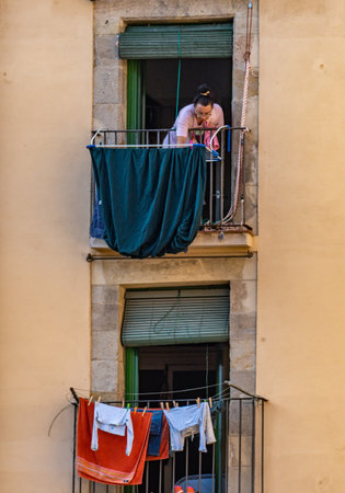 Woman hanging clothes on a balcony in the Gothic quarter of Barcelona. Two vertical windows with hanging clothesのeditorial素材