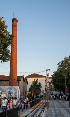 Group of people walking through the entrance of the Viseu fair, with a steam factory column and a tram track that goes up to the top of a hill.のeditorial素材
