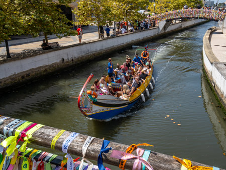 Gondola with tourists navigating the canals of Aveiro with the bridges decorated with strips of colored paperのeditorial素材