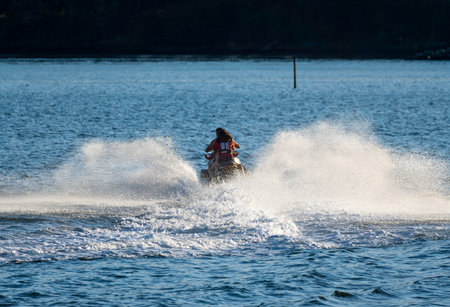 A monitor and a girl on his back and leaving a trail of water foam enjoying the jet ski skidding at high speed along Boiro beach.のeditorial素材