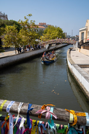 Gondola with tourists navigating the canals of Aveiro with the bridges decorated with strips of colored paperのeditorial素材