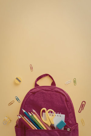 A pink backpack with school supplies, including pencils, scissors, and paper clips, on a yellow background