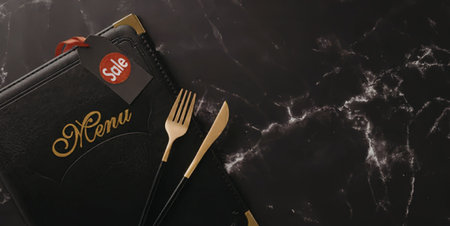 A black pouch with gold writing and a red logo lies on a marble surface alongside gold fork and knife.