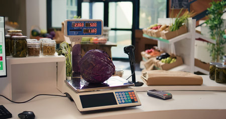 A close-up view of a fresh piece of cabbage on a digital scale in a bright, organized grocery store checkout area with produce and jars in the background.