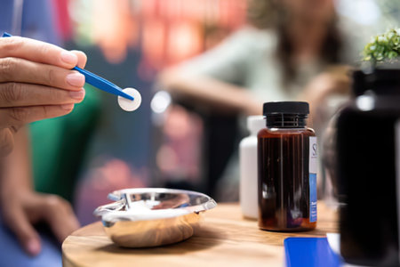 Close-up of a hand using a spoon to scoop sauce from a dark bottle at an outdoor event or market stall.