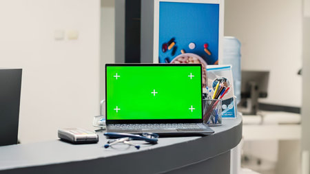 A sleek laptop with a green screen placed on a tidy office desk with stationery and a smartphone nearby.