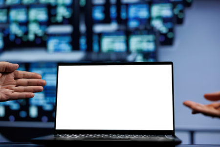 A close-up of hands gesturing towards an open laptop screen on a desk, with a tech-themed digital background showing abstract visuals.