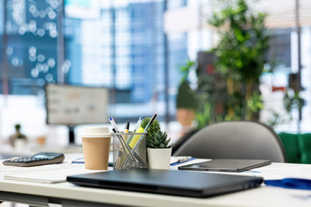 Clean workspace with coffee cup, plant, notebook, and office supplies on a desk near a window.