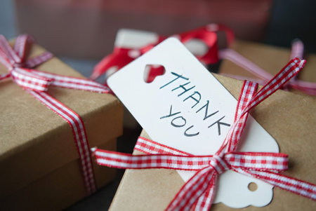 Close-up of a wrapped gift box tied with red ribbon and a handwritten thank you tag.