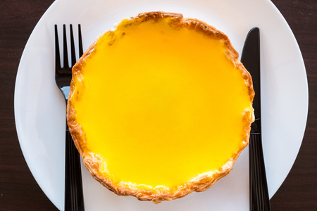 A big cheese tart fill with orange jam ready to eat with fork and knife on white plate on table.