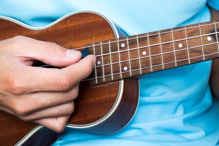 a man is playing ukulele, little guitar. he practice his music skill to become musician for entertain people in concert.の写真素材