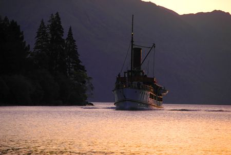 An old steamboat doing its job on mountain lake. Silhouettes of mountains and forest.の写真素材