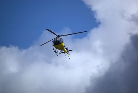 Yellow and blue helicopter flying towards blue sky out of the cloud. Bottom view.