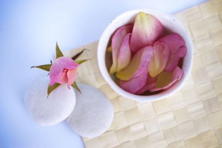 Spa tranquility. Rose bud and petals with pebbles and cup on a cane mat.の写真素材