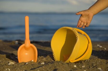 Beach toys and child's hand by the sea shoreの写真素材