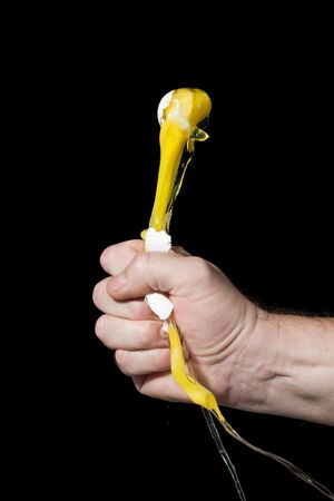 The hand compressed in a fist destroys an egg on a black background. The concept of destruction.の写真素材