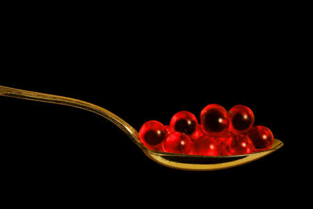 Red pills in a teaspoon, close-up, isolated on blackの写真素材