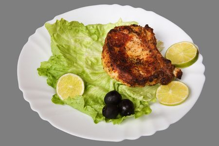 Piece appetizing grilled meat on a plate with a leaf of salad, lemons and olives. Isolated on grey [with clipping path].の写真素材