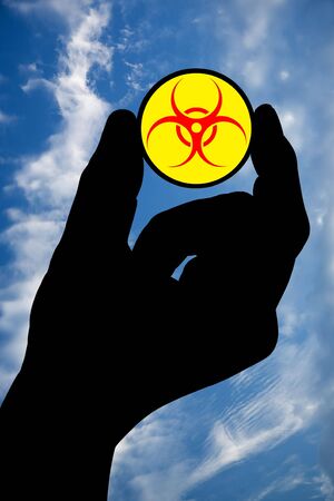 The silhouette of a man's hand holds a biohazard symbol on a background of the sky with clouds. の写真素材