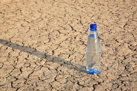 The bottle with cold water with a shadow on the dry cracked groundの写真素材