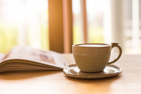 Cup of cappuccino with magazine on the table in the morning,warm tone.