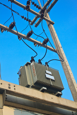 Transformers of an electrical post with power-lines against bright blue skyの写真素材