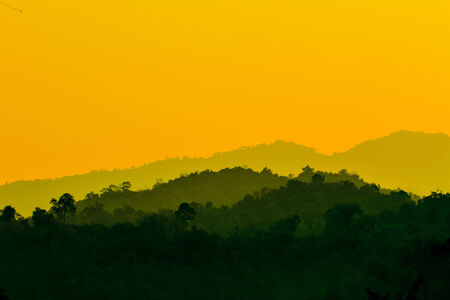 Sun shining through the clouds with silhouetted mountiansの写真素材