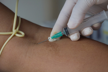 Close-up Of Doctor Injecting Patient With Syringe To Collect Bloodの写真素材