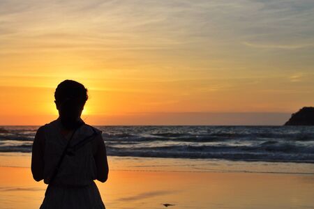 silhouette of a woman on a beach at sunset の素材