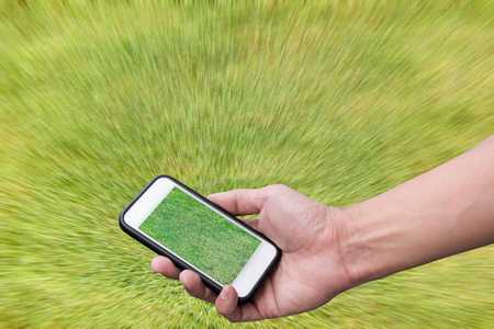Hand holding smartphone with green field on screen,  on green backgroundの写真素材