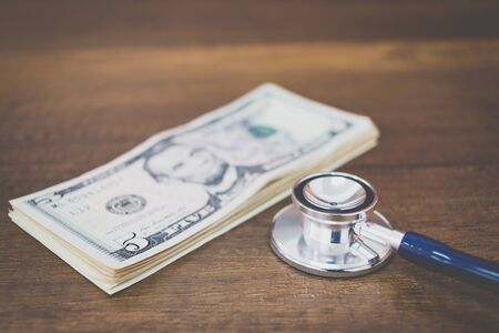 Stethoscope on dollar banknote money on wooden background , Concept of health care costsの写真素材