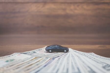Car model on dollar banknotes , cost of buying a car on wooden background