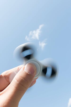 Hands holding popular fidget spinner toy on sky background