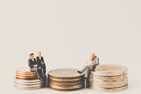 Miniature people business concept sitting on coins with a space for textの写真素材